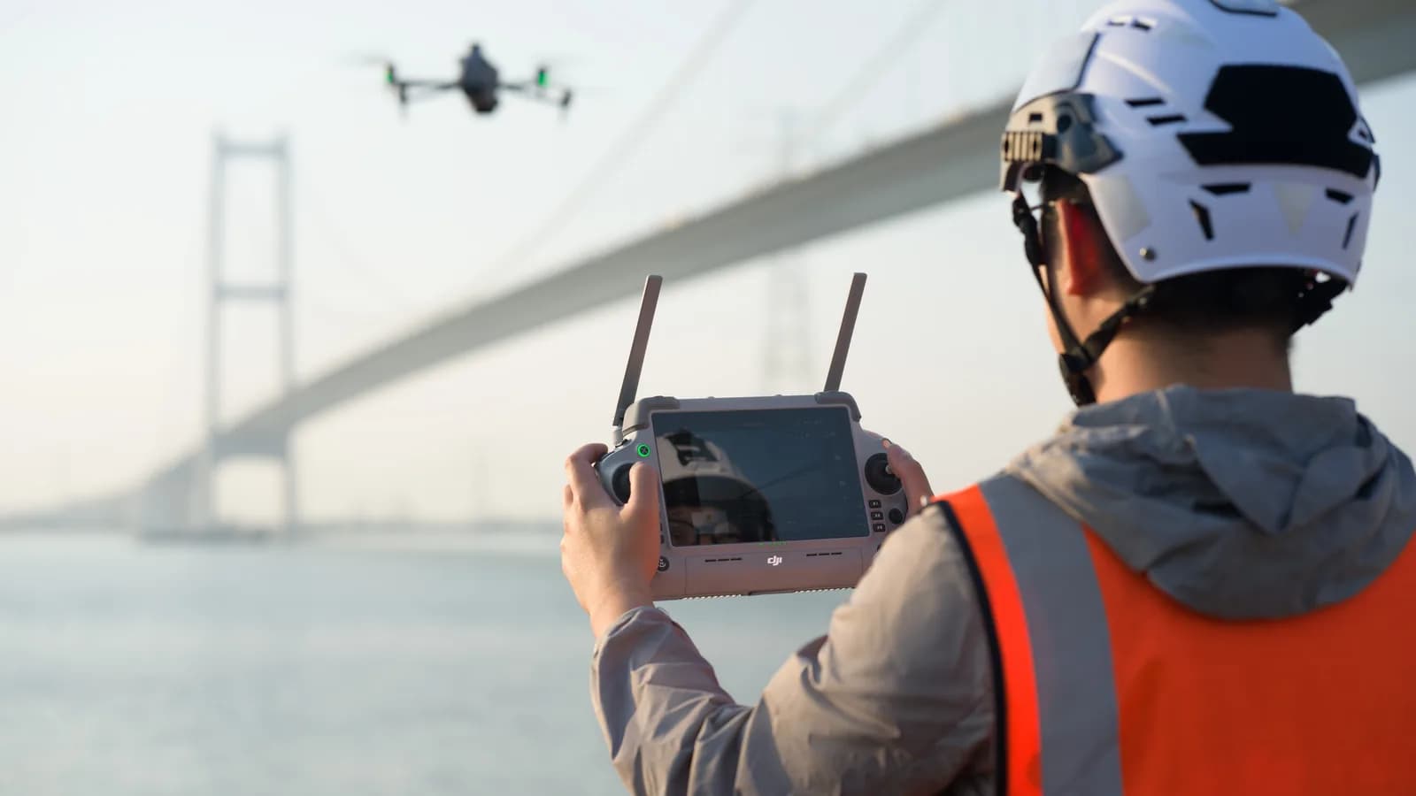 Télépilote en équipement de sécurité pilotant un DJI Matrice 4 près d'un pont suspendu