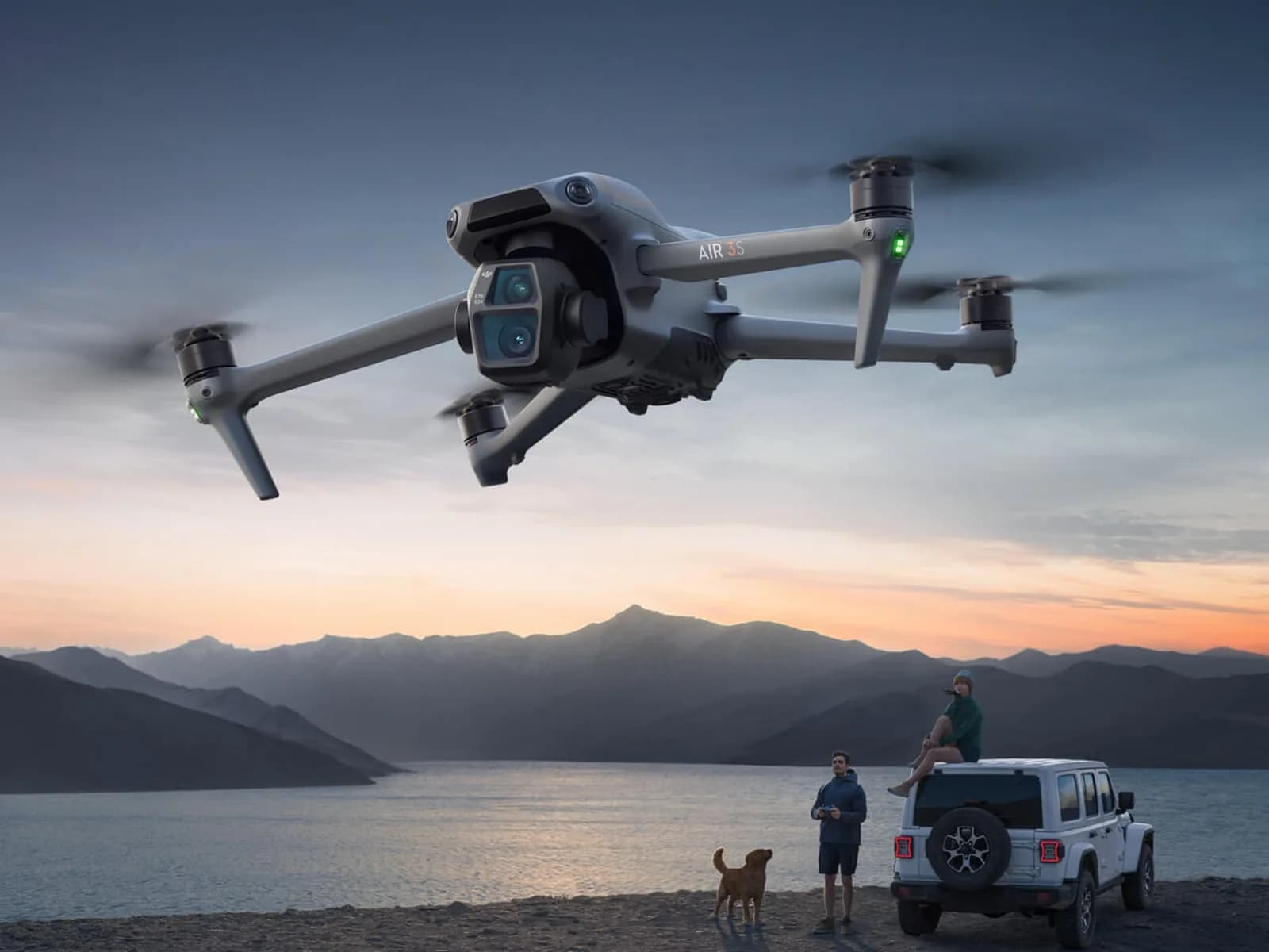 DJI Air 3S en vol au crépuscule au-dessus d'un lac, véhicule garé sur la rive