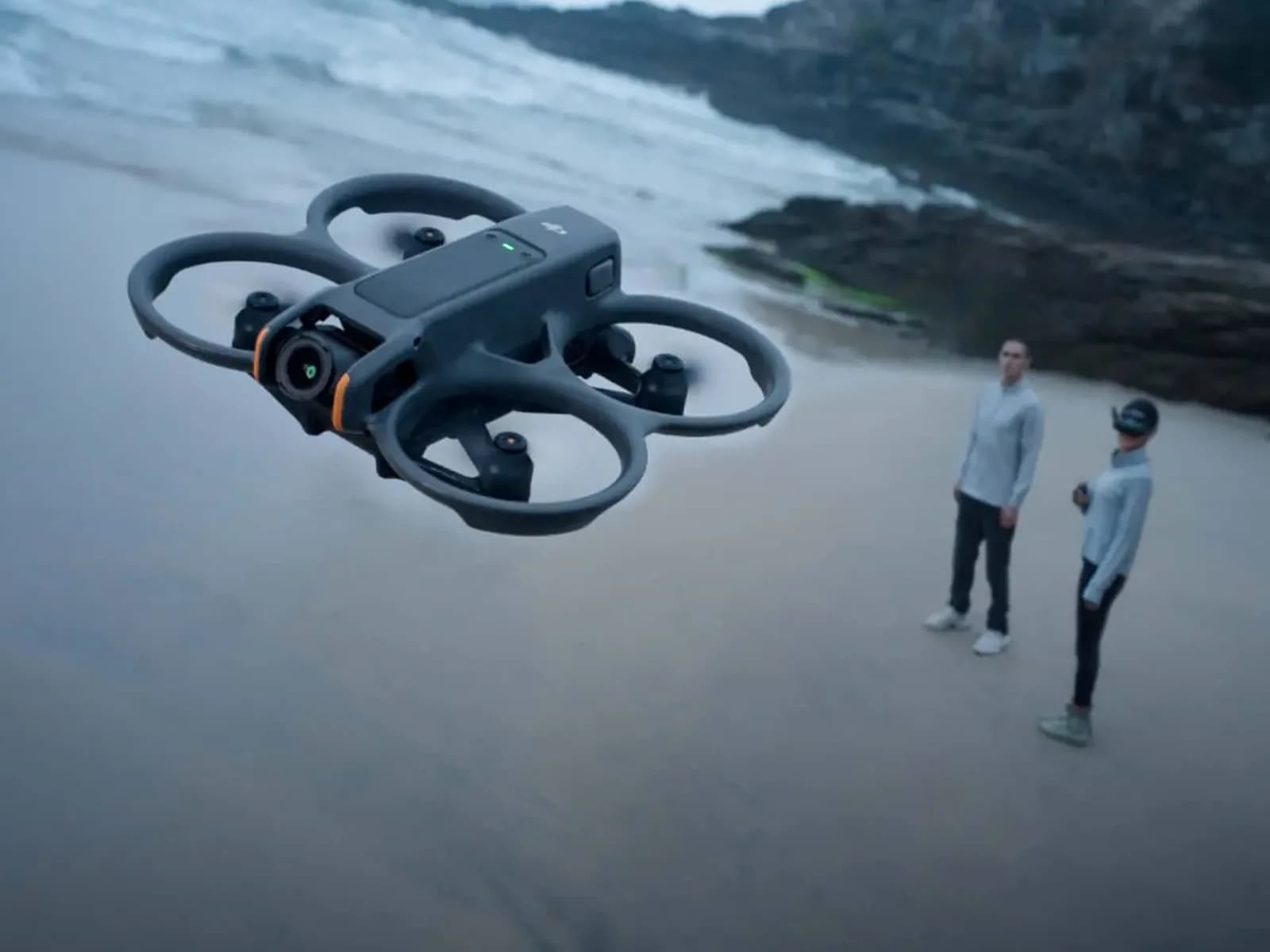 DJI Avata 2 en vol au-dessus d'une plage, deux personnes dont un pilote équipé de lunettes FPV