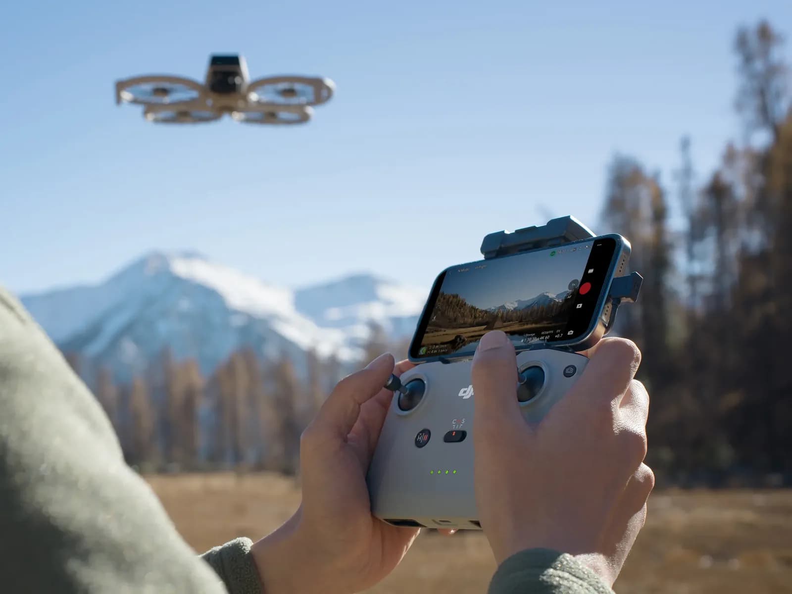 Télépilote pilotant le DJI Flip avec radiocommande et smartphone devant un paysage de montagne