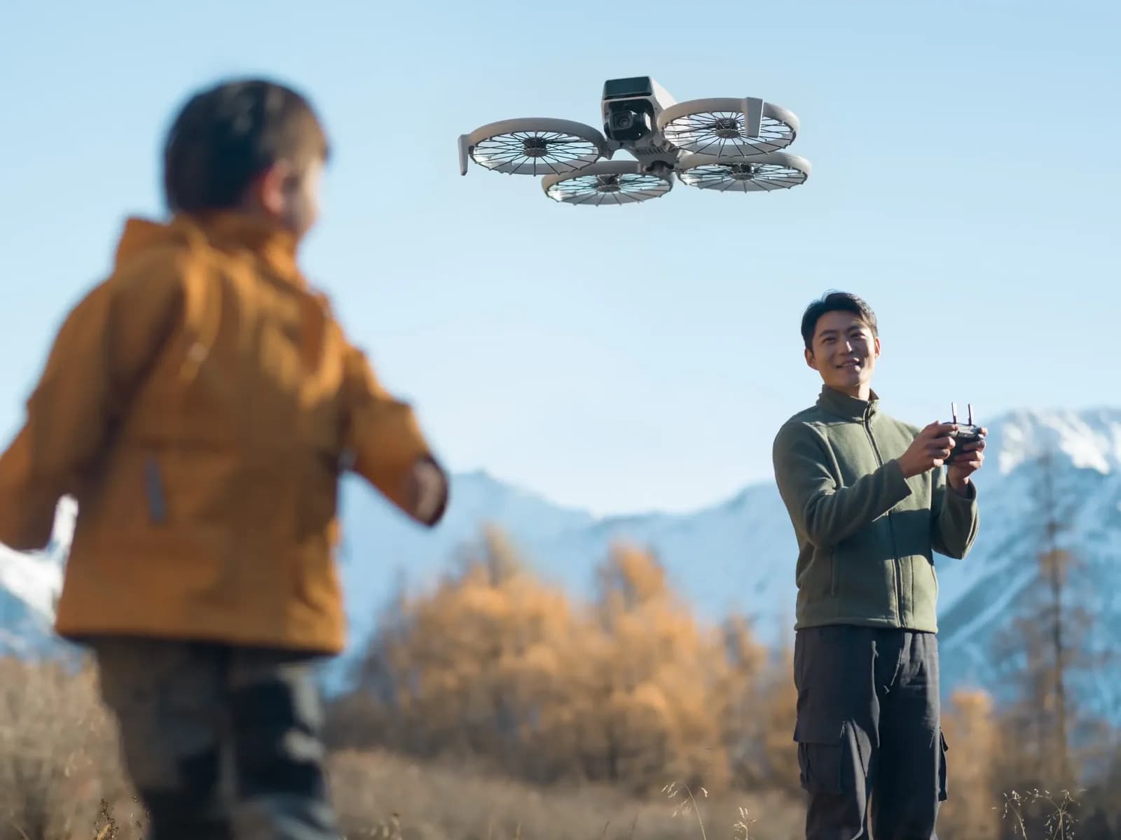 DJI Flip en vol suivant un enfant dans un paysage d'automne, télépilote en arrière-plan