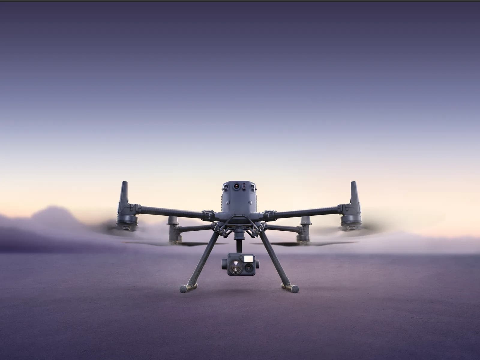 DJI Matrice 350 RTK en vol stationnaire au ras du sol au crépuscule, nacelle caméra sous le châssis