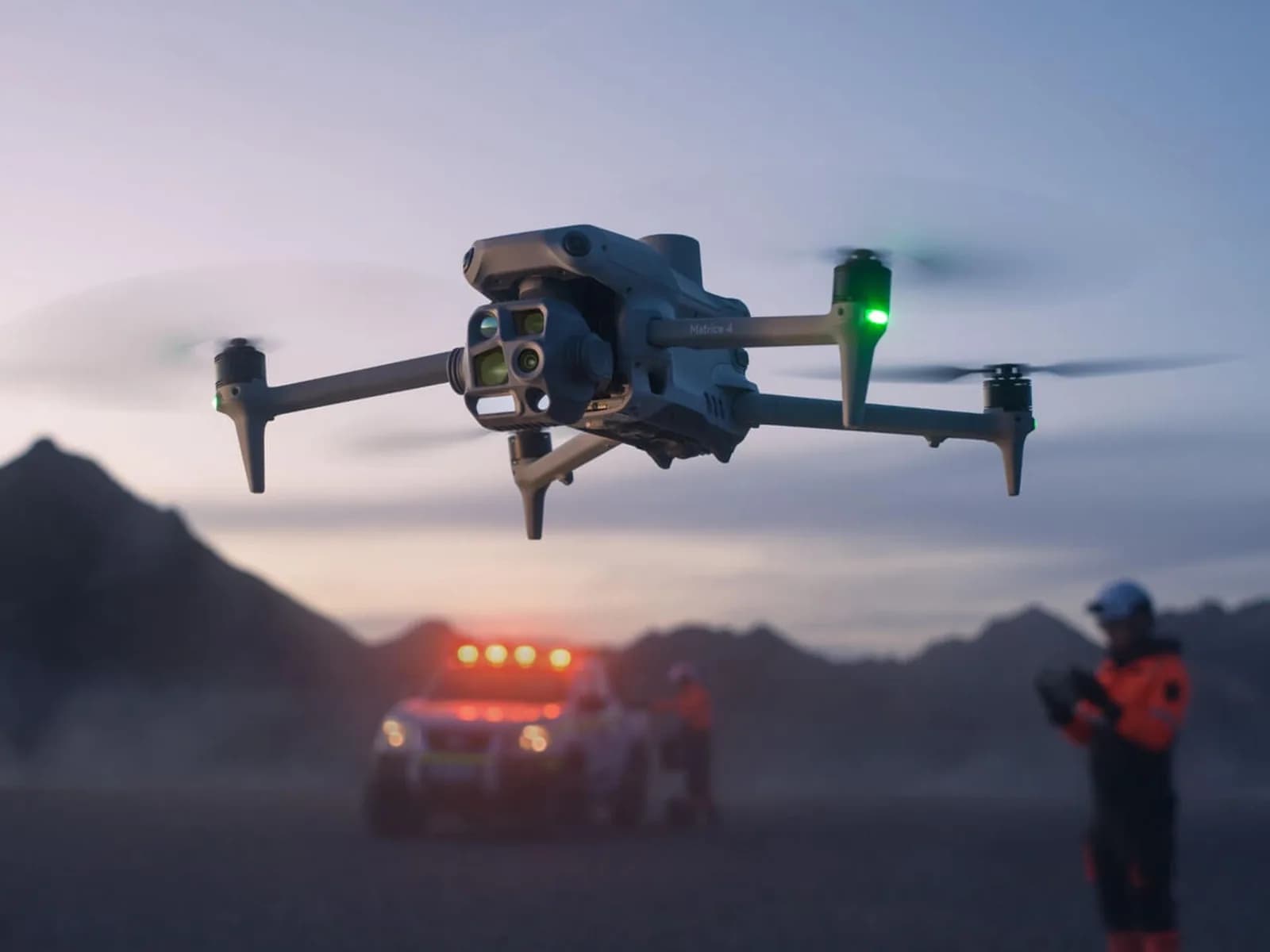 DJI Matrice 4T en vol au crépuscule, télépilote et véhicule de secours gyrophares allumés en arrière-plan