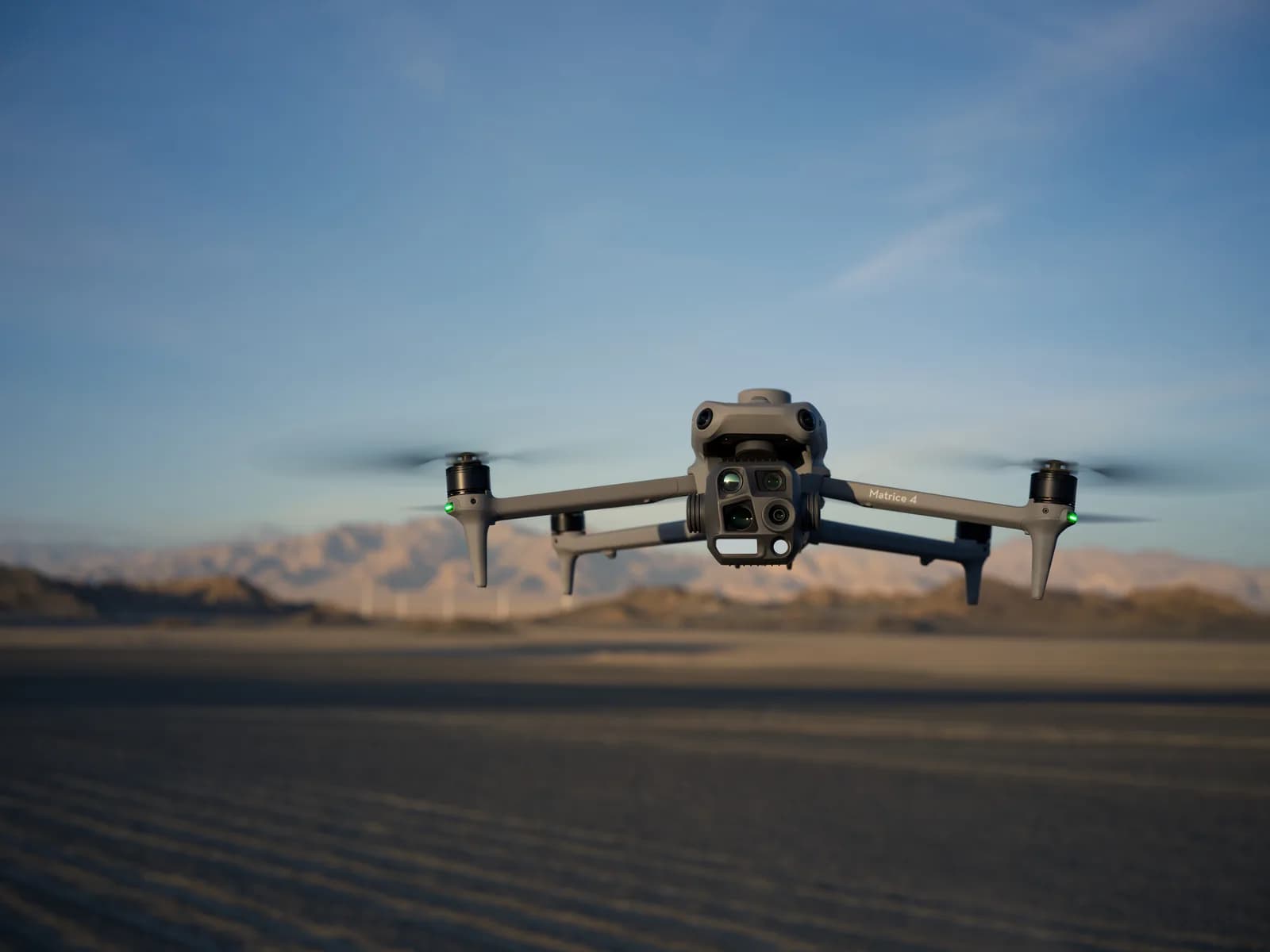 DJI Matrice 4T en vol stationnaire au-dessus d'un sol désertique, nacelle thermique face à l'objectif