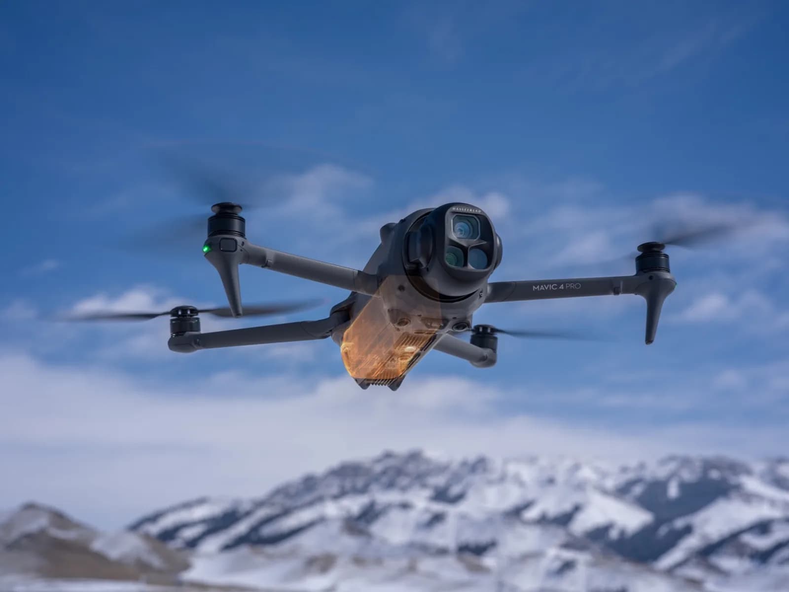 DJI Mavic 4 Pro en vol, triple caméra face à l'objectif, devant des montagnes enneigées