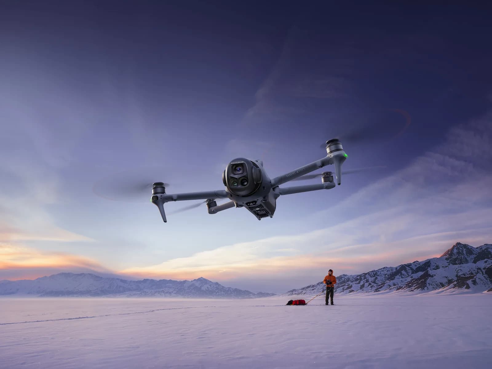 DJI Mavic 4 Pro en vol au crépuscule au-dessus d'une plaine enneigée, télépilote au sol