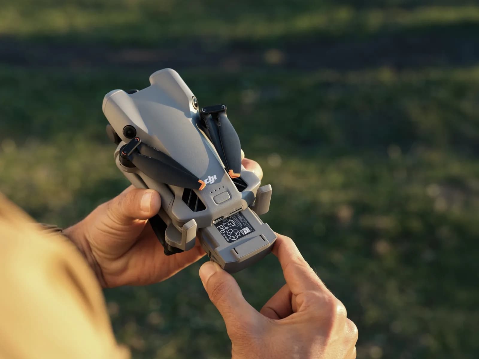 DJI Mini 5 Pro replié tenu dans les mains, batterie en cours d'insertion