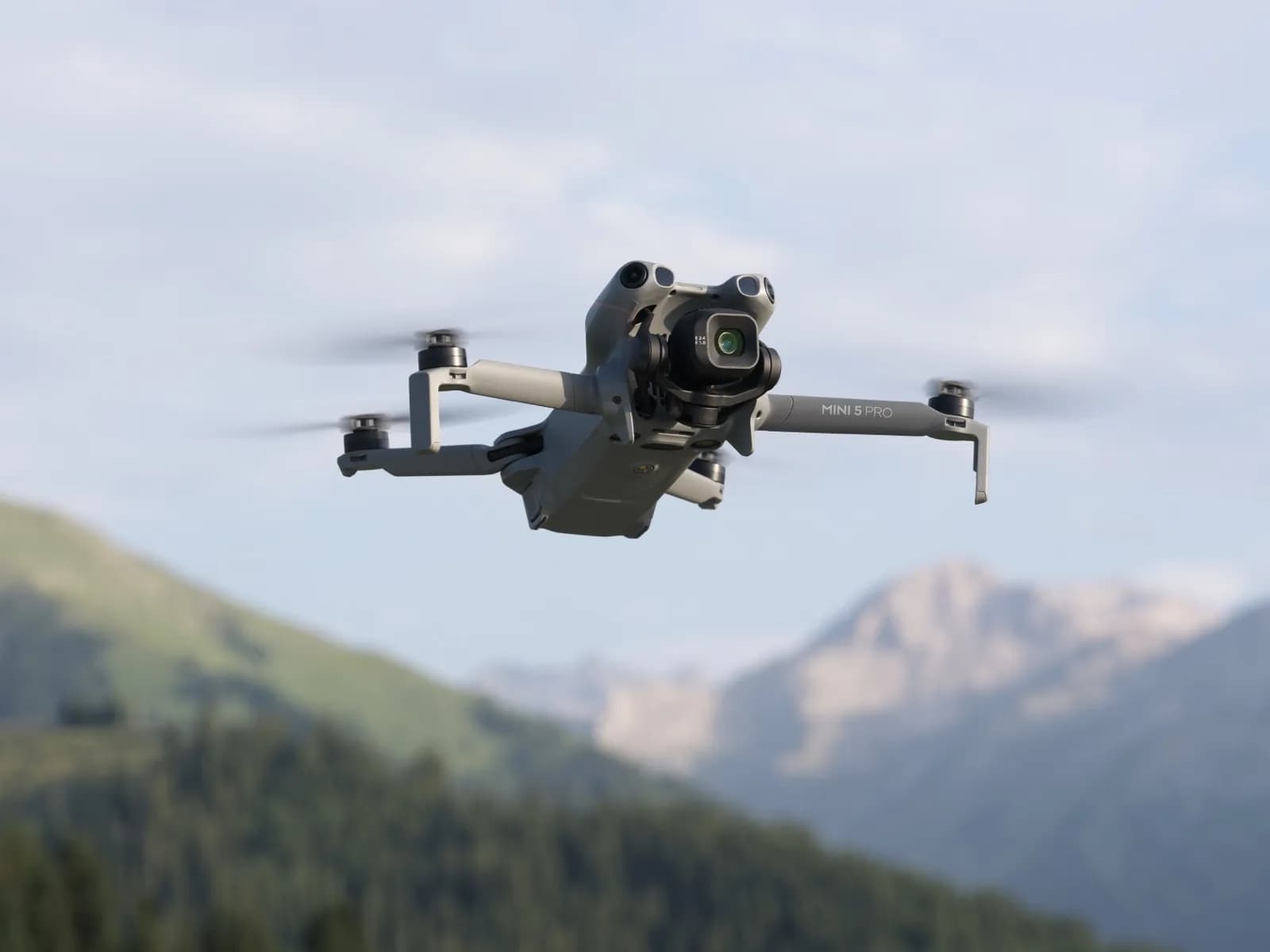 DJI Mini 5 Pro en vol devant un paysage de montagne boisé